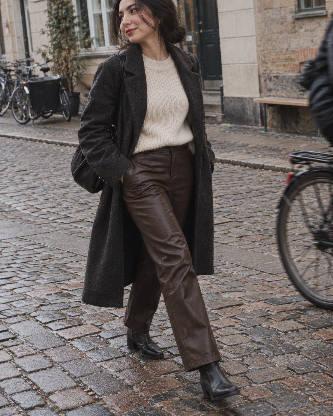 Woman in dark brown leather trousers and a long wool coat crossing a cobbled street