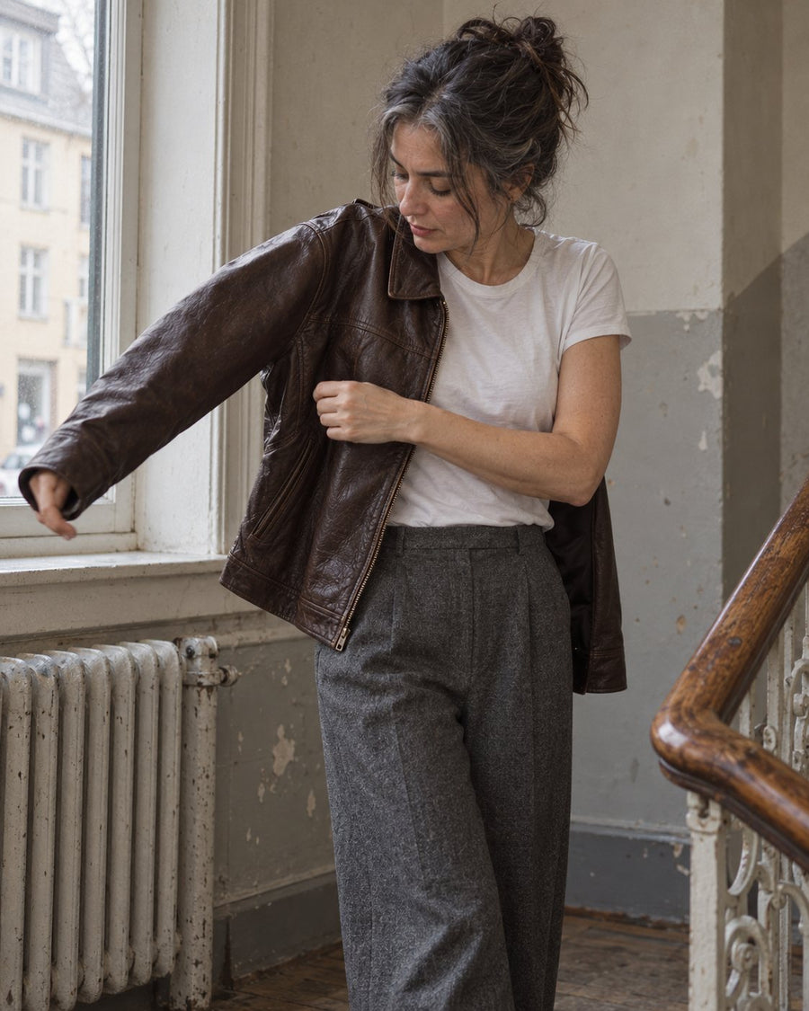 Woman pulling on a dark brown leather jacket on a stairwell landing