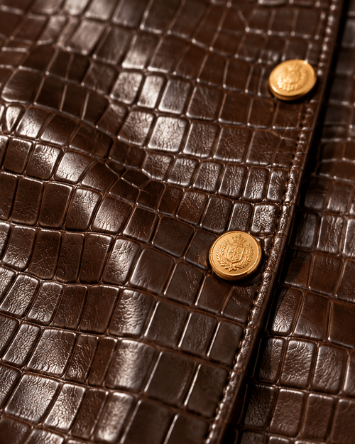 Close-up of chocolate brown croc-embossed leather and gold buttons